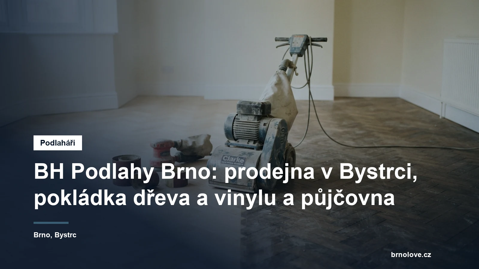 Válcová bruska na parkety uprostřed rozbroušené dubové podlahy, vedle ní role brusného papíru a okrajová bruska